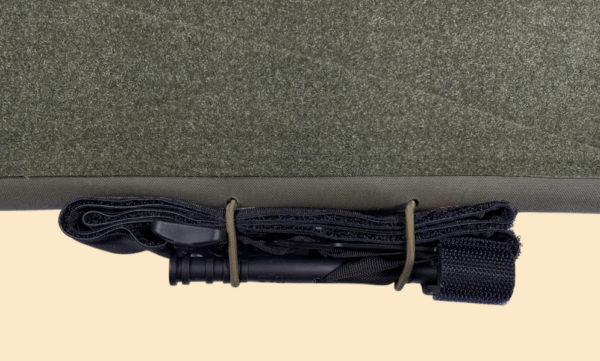 Close-up of a tourniquet displayed on the integrated bungee holes on the bottom of a chest rig placard.